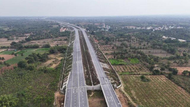 Wide cinematic aerial of a new highway corridor showcasing long uninterrupted roadways, open landscapes, and surrounding agricultural terrain, emphasizing scale, connectivity, and modern infra