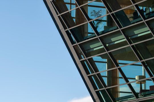 glass canopy cuts across blue sky above office facade, where windows, reflection and urban architecture form a clean corporate detail