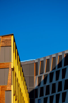 yellow facade meets blue sky beside geometric office building, where urban architecture, windows and sharp angles create a bold exterior view
