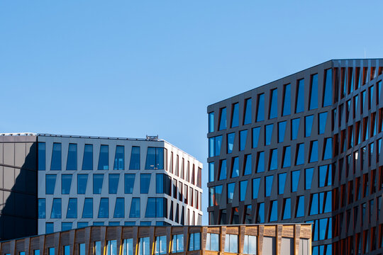 urban office buildings lean across blue sky as angled facade, glass windows and geometric architecture create a crisp corporate district view