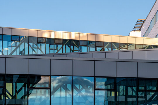 glass office walkway spans between buildings under blue sky, with reflection, facade and urban architecture creating a layered corporate exterior