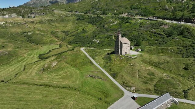 Aerial view of the historic Alter Spittel building at Simplon Pass surrounded by green alpine slopes and winding mountain roads in Simplon, Valais, Switzerland.