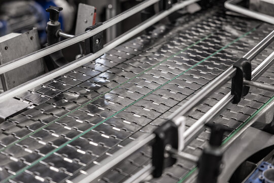 Close-up of metal conveyor belt with guide rails in a brewery packaging or bottling line, showing industrial automation equipment