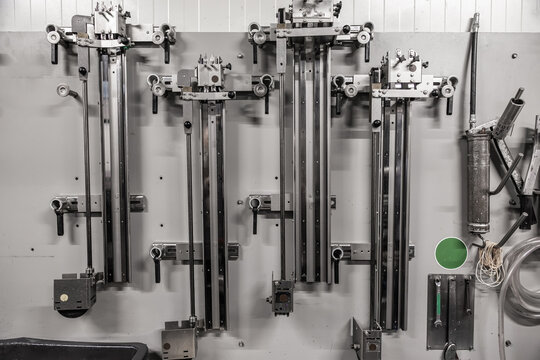 Wall-mounted brewery packaging or bottling equipment with metal rails, handles, hoses, tools, and adjustment mechanisms in a production area