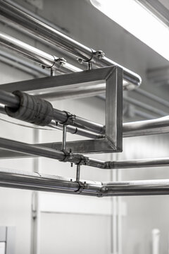 Black and white view of overhead stainless steel pipes, clamps, and support frame inside a brewery production area, with ceiling lights and copy space