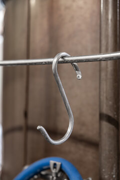 Close-up of a metal hook hanging from a rod inside a brewery or industrial processing area, with blurred tank background and copy space