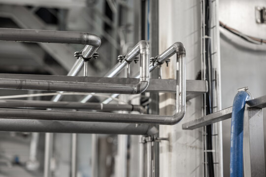 Stainless steel pipes and railings inside a brewery production facility, with blurred industrial background and copy space
