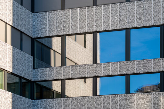 horizontal architecture detail frames stone and glass windows on an urban building facade, where reflection sits between textured exterior bands