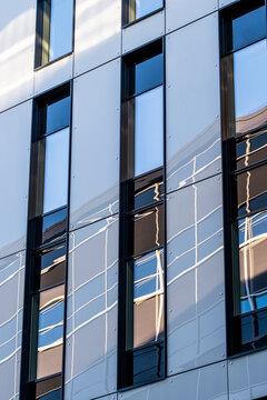 vertical panels divide glass windows across an urban building facade, where architecture and abstract reflection stretch through narrow mirrored surfaces