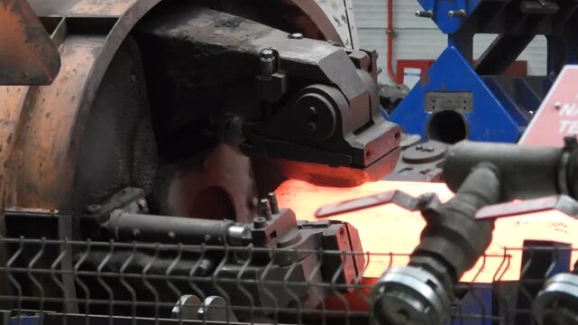 A forging machine processes a red-hot steel ingot in a large steelworks.