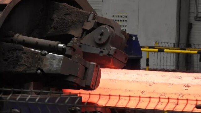 A forging machine processes a red-hot steel ingot in a large steelworks.