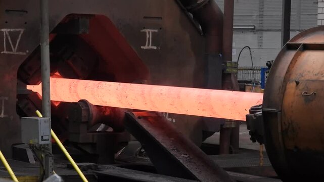 A forging machine processes a red-hot steel ingot in a large steelworks.