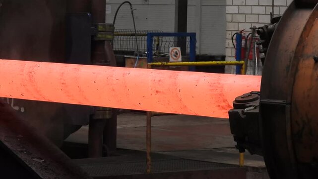 A forging machine processes a red-hot steel ingot in a large steelworks.