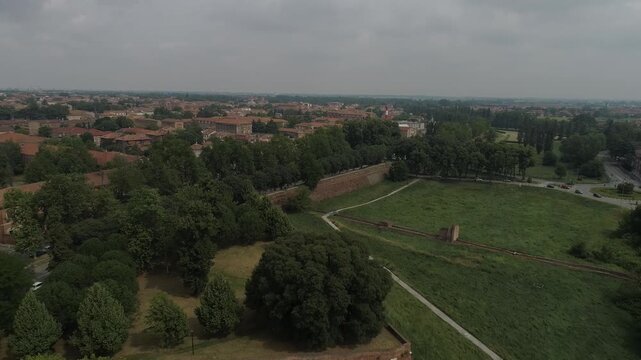 Aerial view of the historic city walls and lush green fields surrounding the old town under a cloudy sky in Ferrara, Emilia-Romagna, Italy.