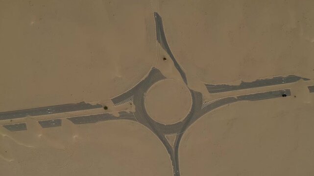 Aerial view of a road roundabout and asphalt streets partially covered by shifting sand dunes in the desert Dubai, Dubai, United Arab Emirates.