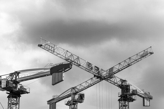 in black and white, construction cranes cross the sky above an urban building site, turning development and architecture into silhouettes