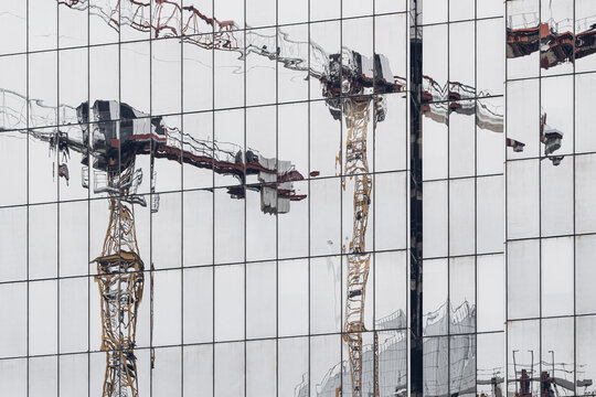 across the glass facade, crane reflection turns construction and urban building site architecture into a fragmented city pattern of mirrored lines