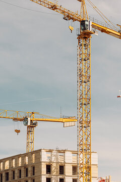 yellow construction cranes lift over a city building site, where urban development, tower form and architecture meet a pale sky above masonry