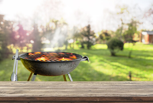 Wooden table with blurred barbecue grill in backyard garden