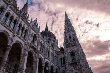 Hungarian parliament building in budapest seen from a low angle against a dramatic cloudy sky, highlighting its ornate gothic revival dome, spires, turrets and detailed stone façade © bestforbest