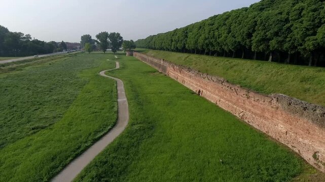 Aerial view of the ancient city walls surrounded by lush green trees and a walking path in Ferrara, Emilia-Romagna, Italy.