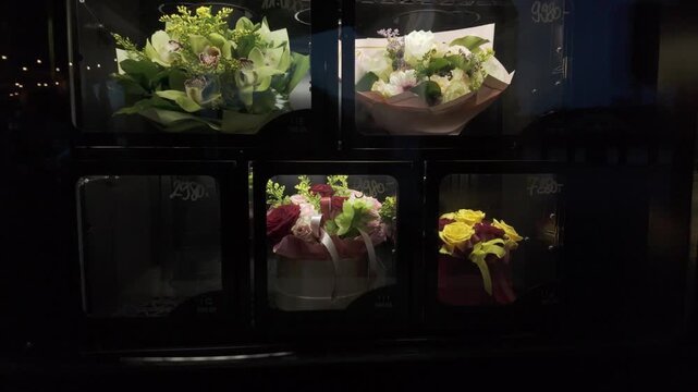 Flower vending machine at night. Bouquets made of fresh colourful flowers behind glass doors of a dispensing machine. Innovative and modern 0-24 last minute shopping concept. Dolly in slow motion.