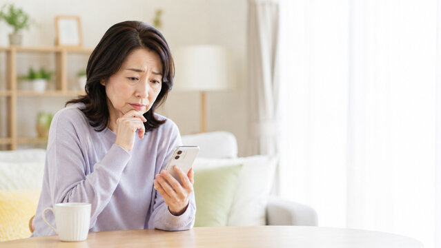 スマホを見ながら不安そうに考える中高年女性