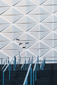 white geometric facade rises above stairs and blue railings, where urban architecture, pattern and clean exterior lines meet a bright public entrance