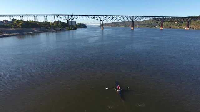 Aerial view of a lone rower in a scull on the calm waters of the Hudson River with the Walkway Over the Hudson bridge in the background Poughkeepsie, New York, United States.