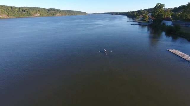 Aerial view of a single scull rower on the Hudson River near the Hudson River Rowing Association building with lush hills in Poughkeepsie, New York, United States.