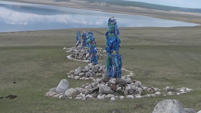 Azure prayer flags flutter upon ancient stone Oboos overlooking the serene expanse of Lake Khuvsgul in Mongolia. A tranquil landscape honors deep spiritual traditions.