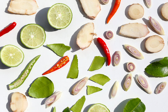 A colorful, close-up pattern of Thai herbs: lime slices, galangal, lemongrass, chilies, and kaffir lime leaves.