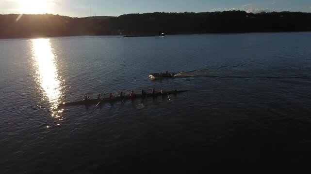Aerial view of rowers in a scull boat followed by a motorboat on the Hudson River during a golden sunset in Poughkeepsie, New York, United States.