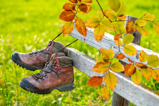 Ein Paar Wanderstiefel aus Leder h&auml;ngen mit Herbstlaub an einem h&ouml;lzernen Zaun  im Allg&auml;u - FOTOMONTAGE