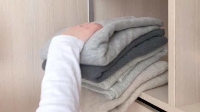 A woman takes winter clothes out of the closet. Women's hands take wool sweaters from the shelf. The change of season, when warm clothes once again become a necessary part of everyday life