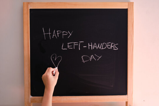Child's left hand writing happy left-handers day on blackboard