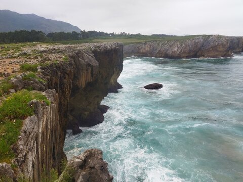 Acantilados escarpados y olas rompiendo en los Bufones de Pr&iacute;a, Llanes, Asturias. Paisaje costero salvaje del Mar Cant&aacute;brico en un d&iacute;a nublado.