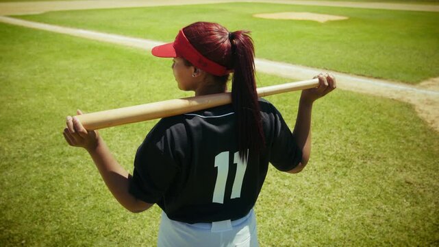 A focused young baseball player stands on the diamond, bat on her shoulder, ready to play. She looks across the field, anticipating the next play.