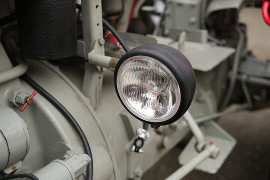 Industrial machine close up showing headlamp, metal frame and wires, highlighting lens detail, bolts and rugged equipment in a workshop setting