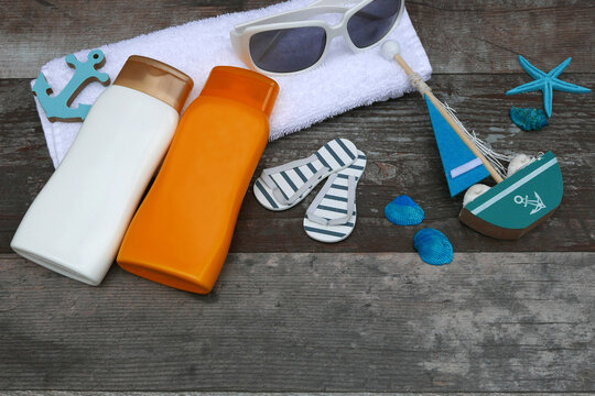 Strandaccessoires darunter Sonnencreme, Sonnenbrille und ein Handtuch  auf einem Holzuntergrund.