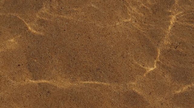 Crystal clear swimming pool water casting shimmering caustic light reflections across a textured sandy bottom, creating a relaxing and serene aquatic atmosphere.