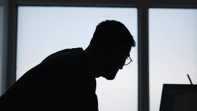 Individual Focused On Computer At Night. Person Hunched Over Laptop In Quiet Evening Environment. Media