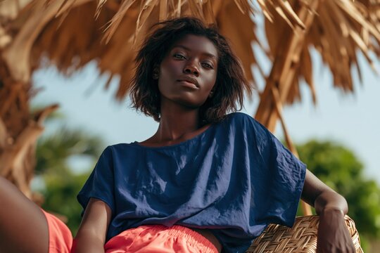 Relaxed tropical outdoor portrait of young woman in wicker chair with blue top and coral skirt for lifestyle background and banner design