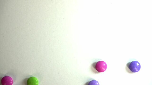 A close-up, high-key shot of colorful candy-coated chocolate drops scattered on a bright white background, creating a playful and vibrant aesthetic for food and lifestyle marketing.