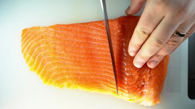 A professional close-up of a chef slicing a fresh salmon fillet on a white cutting board, showcasing culinary precision and the vibrant, healthy texture of the raw fish.
