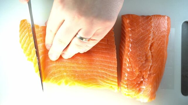 A professional close-up of a chef slicing a fresh salmon fillet on a white cutting board, showcasing culinary precision and the vibrant, healthy texture of the raw fish.