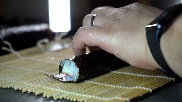 A close-up shot of a chef's hand rolling fresh sushi on a bamboo mat, showcasing the precision and artistry of Japanese culinary craft.