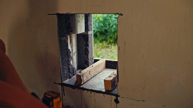 A Person is Drilling Into a Wooden Plank to Secure it Around a Small Rectangular Wall Opening - Close Up
