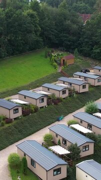 High angle cinematic shot of a resort featuring rows of modern mobile houses and cabins nestled in the green landscape of Kaszuby, Poland. Useful for travel and real estate themes.