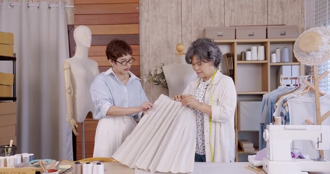 Adult asian daughter sewing pleated fabric boutique studio fashion teamwork family business designer seamstress tailor handmade textile entrepreneurship clothing garment pattern making apparel atelier